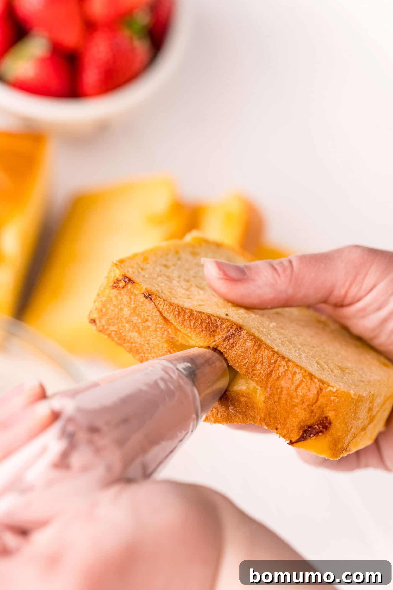 A piping bag, filled with strawberry cream cheese, being carefully inserted into the prepared slit in the brioche bread.