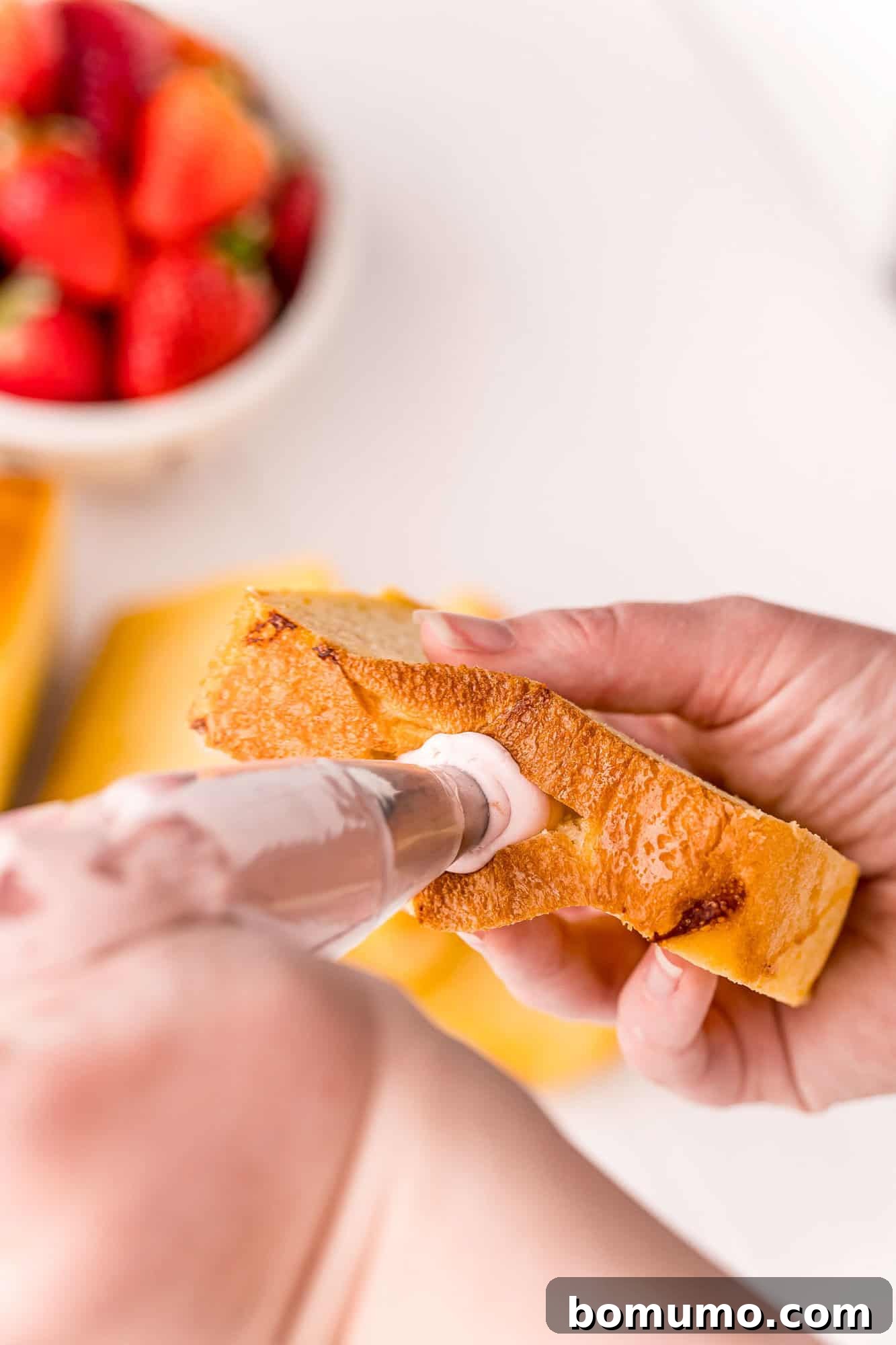 Close-up shot of the creamy strawberry cream cheese filling being piped into a thick slice of brioche bread.