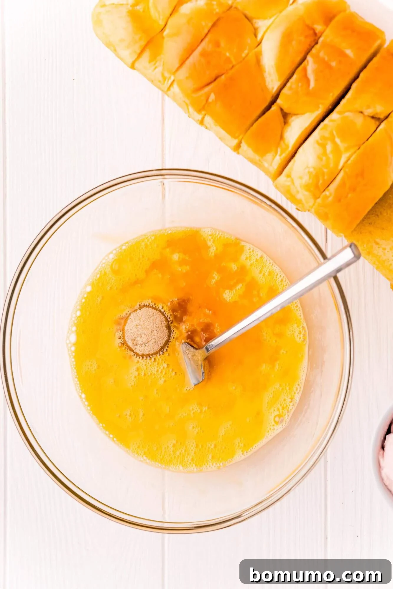Brown sugar being sprinkled into the beaten egg mixture in a glass bowl.