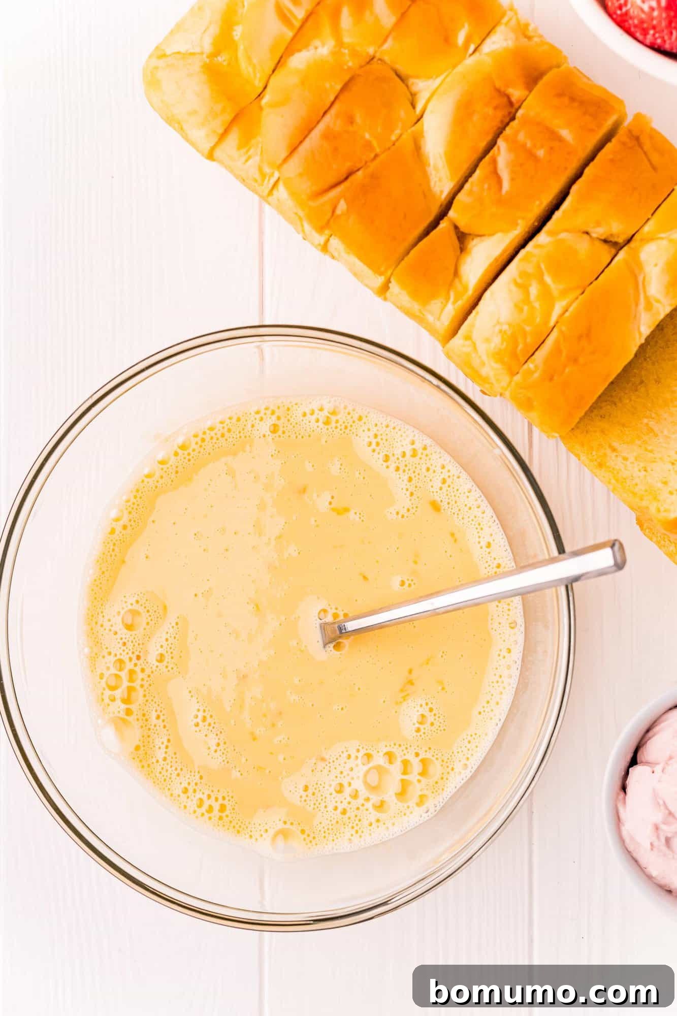 The completed egg custard mixture, featuring eggs, milk, sugar, and vanilla, perfectly blended in a mixing bowl.