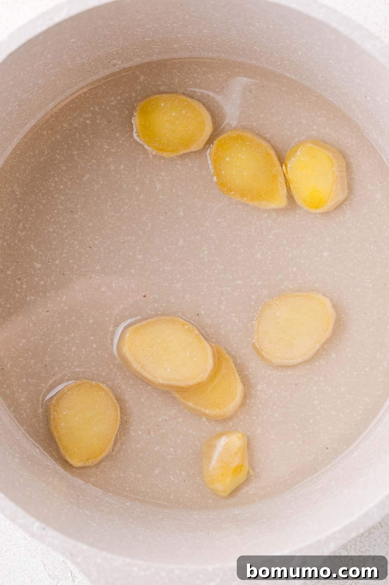 Crimson Sunset Sip 4 Sliced ginger pieces gently simmering in a pot of simple syrup, infusing flavor.