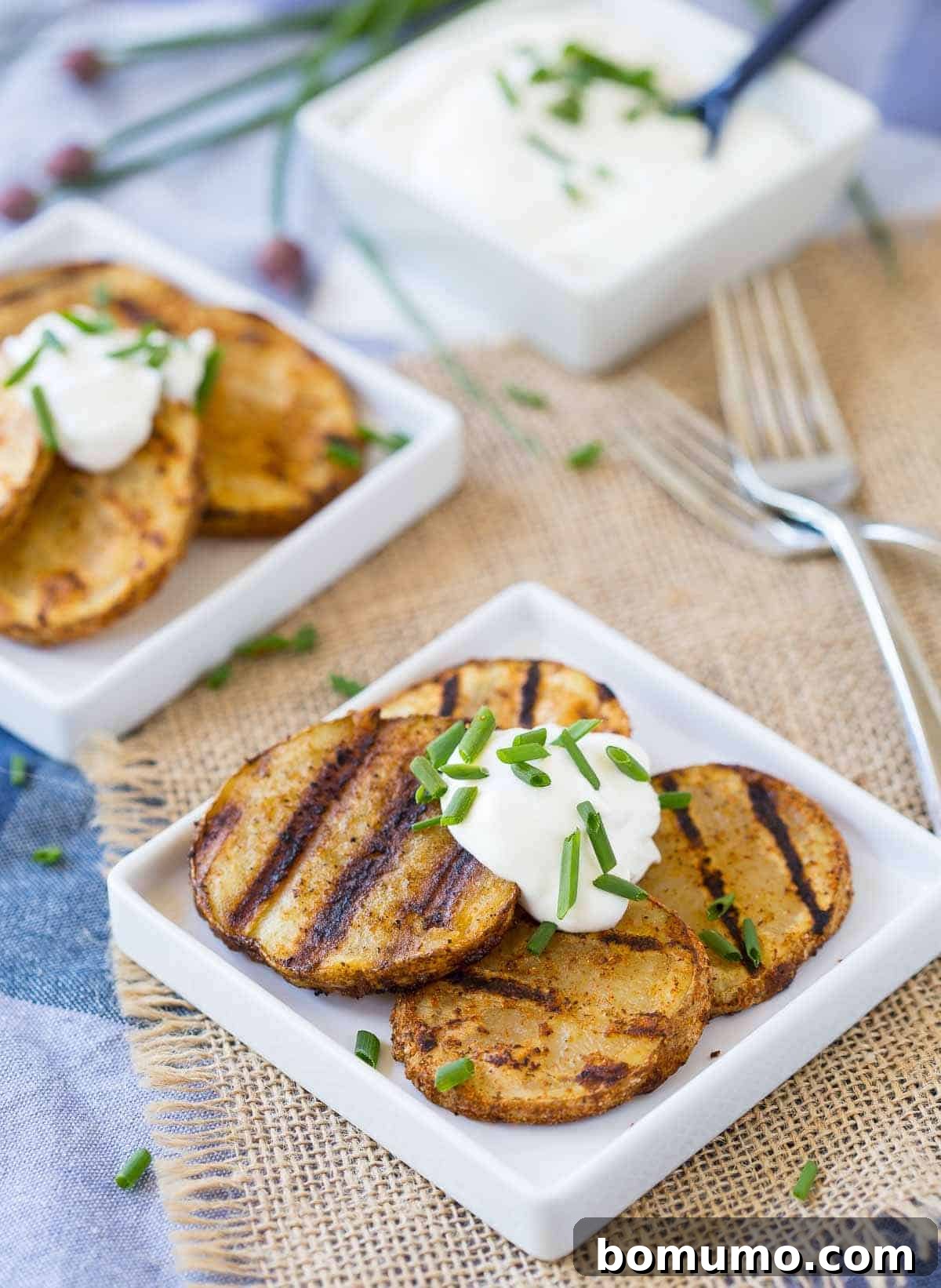 Four potato slices on square white plate, topped with sour cream and chopped chives.