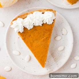 A perfectly sliced homemade pumpkin pie, viewed from above, adorned with a swirl of fresh whipped cream.
