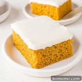 A luscious pumpkin bar topped with generous cream cheese frosting, served on a pristine white plate.