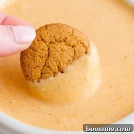 A crisp gingersnap cookie being dipped into a bowl of irresistibly creamy pumpkin dip, ready for a fall party.