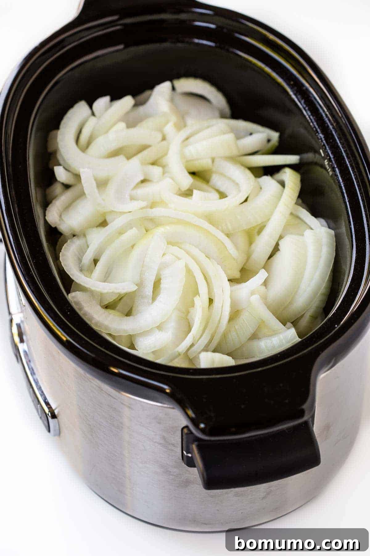 Uncooked, thinly sliced onions generously filling a slow cooker pot, ready for the caramelization process.