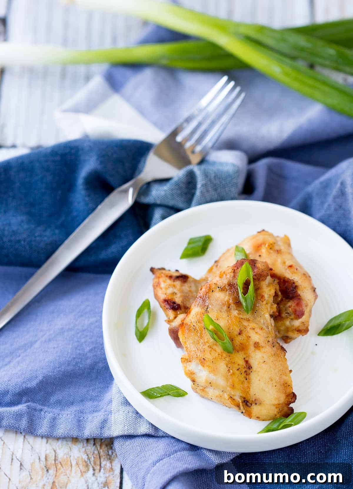 Overhead shot of perfectly grilled chicken thighs on a small white plate, elegantly garnished with freshly sliced green onions, ready to be enjoyed.