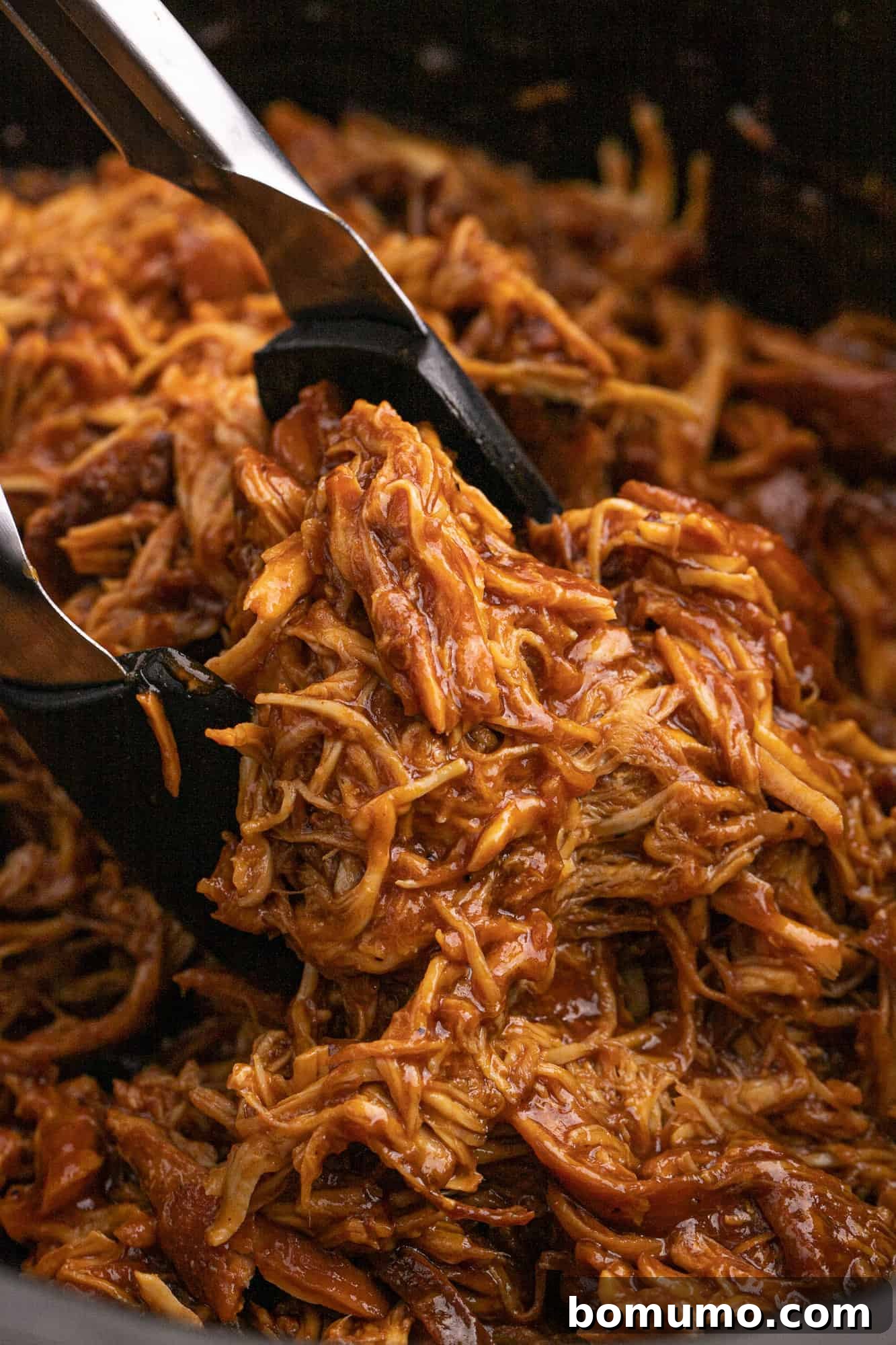 Slow Cooker BBQ chicken between tongs.