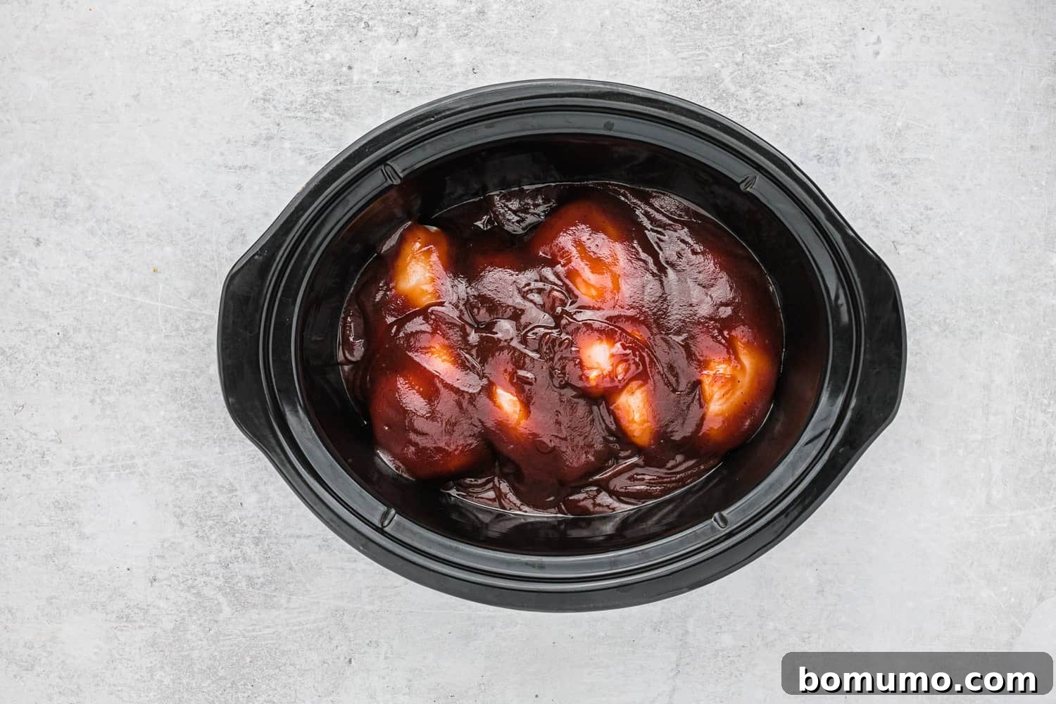 Uncooked chicken and bbq sauce in a slow cooker.