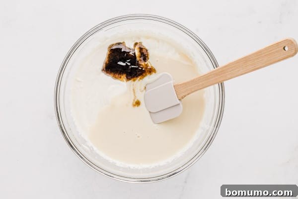 Homemade vanilla ice cream is easy to make with only 3 ingredients! This no-churn ice cream recipe is so creamy, made with real vanilla bean. Sweetened condensed milk and vanilla bean paste being gently folded into the freshly whipped heavy cream in a glass bowl.