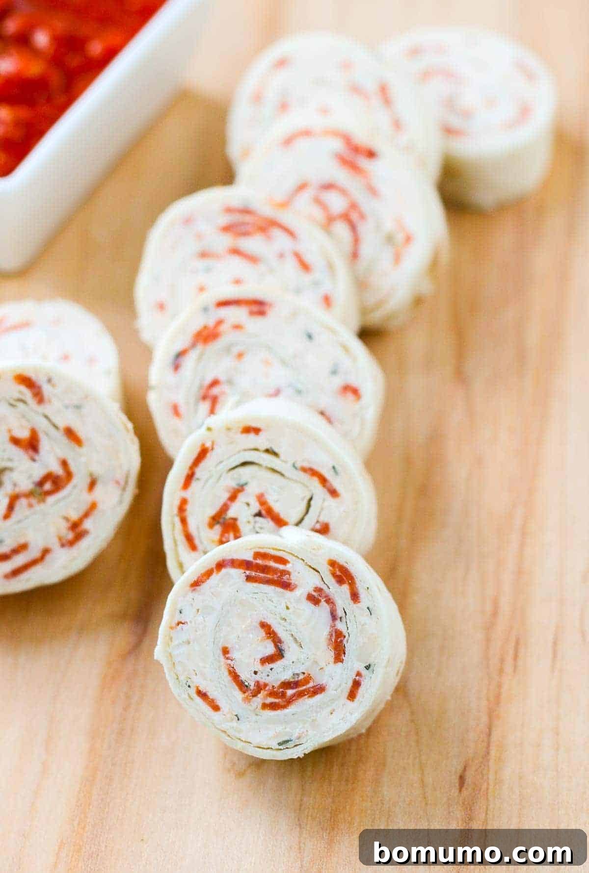 Quick Pepperoni Pizza Roll-Ups 2 Vibrant pepperoni pizza tortilla pinwheels neatly arranged on a rustic wooden board, ready to be served.