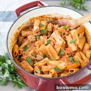 Overhead view of rigatoni pasta in a red Dutch oven, garnished with fresh herbs and ready for serving.