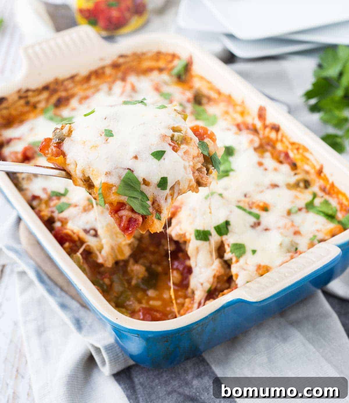 A vibrant One-Dish Italian Chicken and Rice Bake in a blue stoneware baking dish, with a serving being lifted out by a spoon, showcasing tender chicken, rice, and melted cheese.