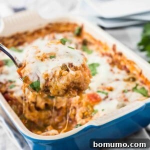 A delicious and bubbly baked casserole in a blue baking dish, with a serving spoon poised to lift out a portion of Italian chicken and rice.