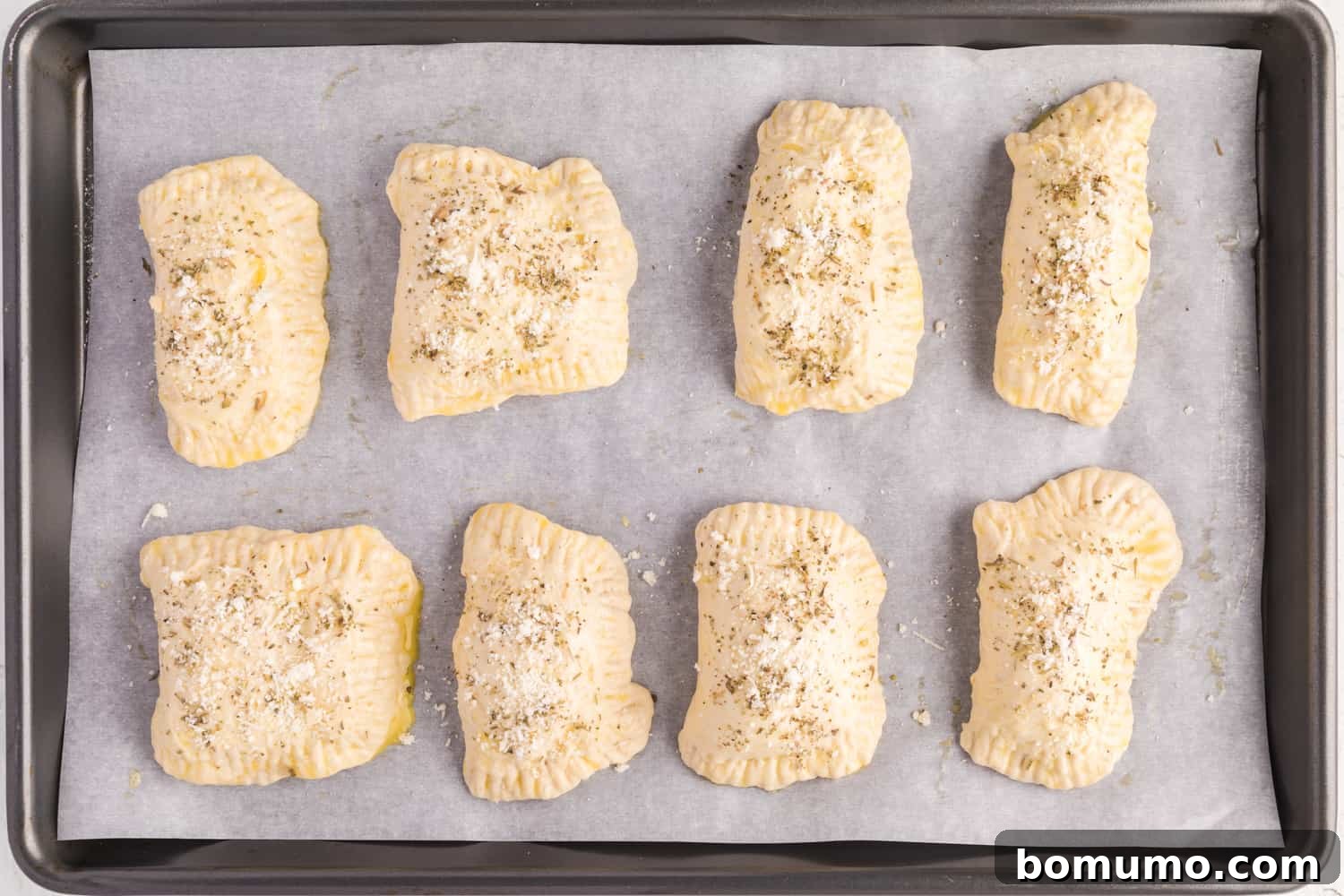 Unbaked pepperoni pizza hot pockets on a sheet pan, brushed with egg wash and ready for the oven.
