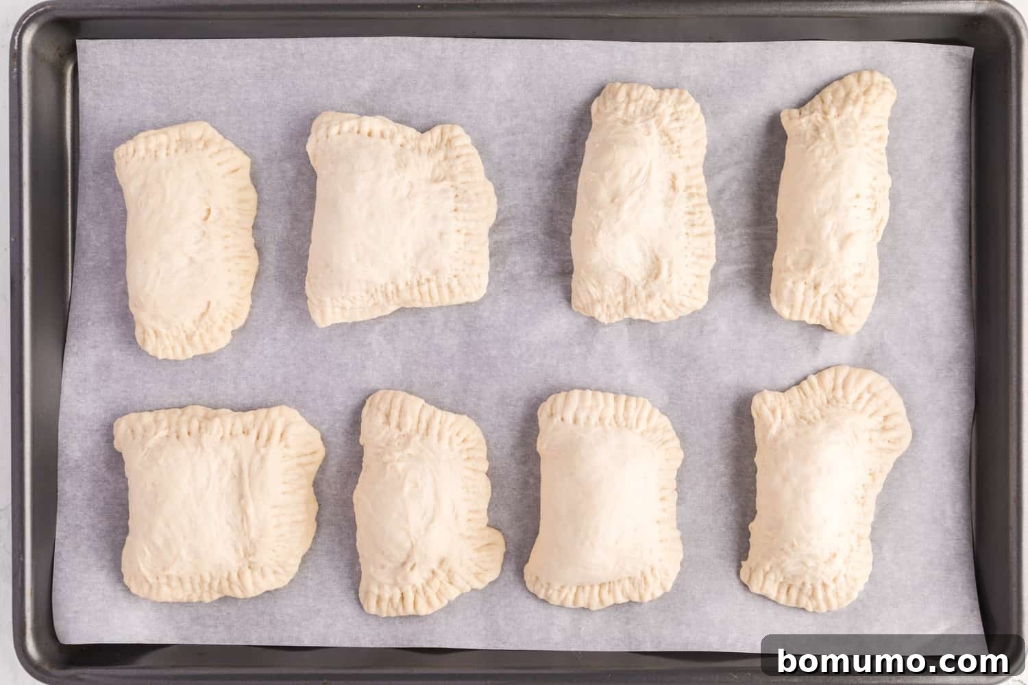 Multiple unbaked hot pockets neatly arranged on a sheet pan, waiting for the oven.