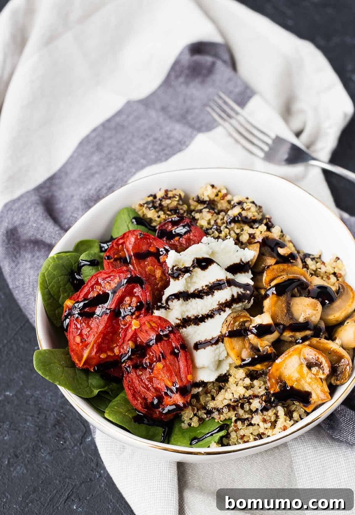Overhead shot of a vibrant Quinoa Bowl with roasted tomatoes, creamy ricotta, sautéed mushrooms, fresh spinach, and a drizzle of rich balsamic glaze.
