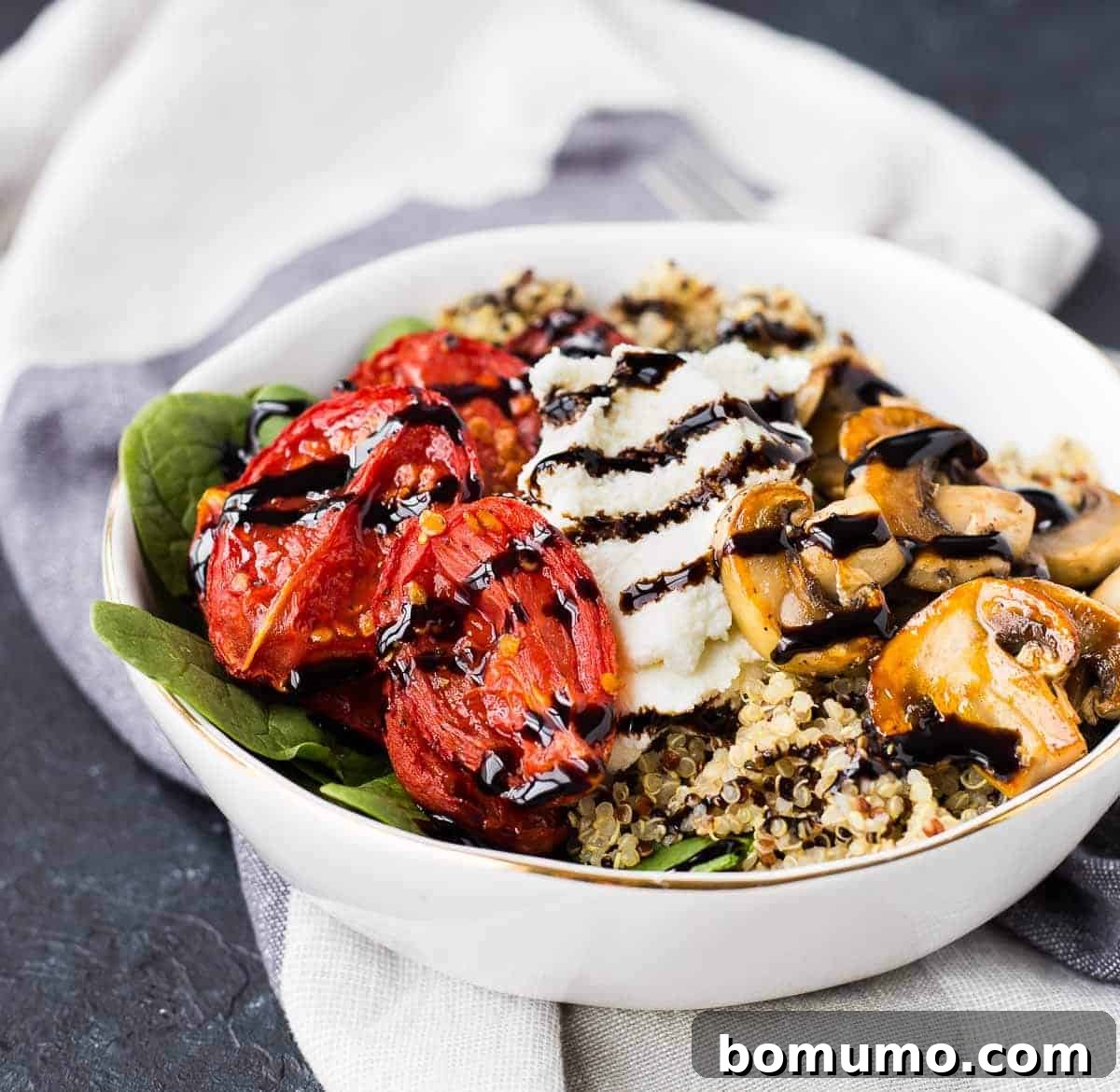 A close-up, front view of a vibrant Quinoa Bowl, beautifully presented on a white linen dish towel.