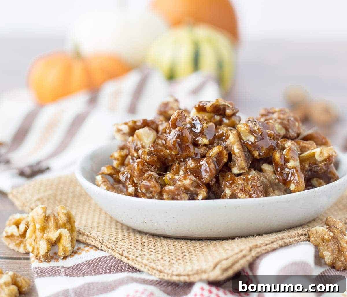 A close-up shot of a rustic bowl brimming with glossy pumpkin spice candied walnuts, positioned on a wooden surface with a soft focus on autumn decor in the background.