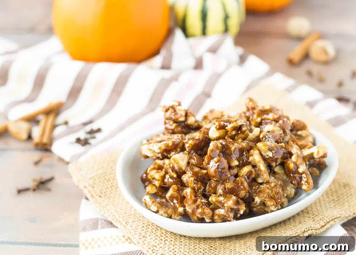 A charming bowl of pumpkin spice candied walnuts sits on a wooden table, adorned with festive orange pumpkins in the soft focus background, creating an inviting autumn scene.
