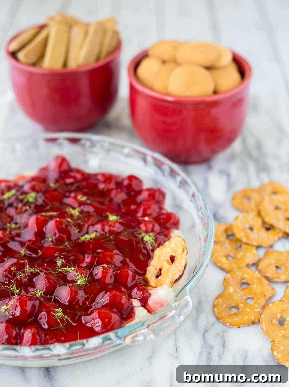A pretzel being dipped into a luscious cherry cheesecake dip, highlighting the delightful salty-sweet combination.