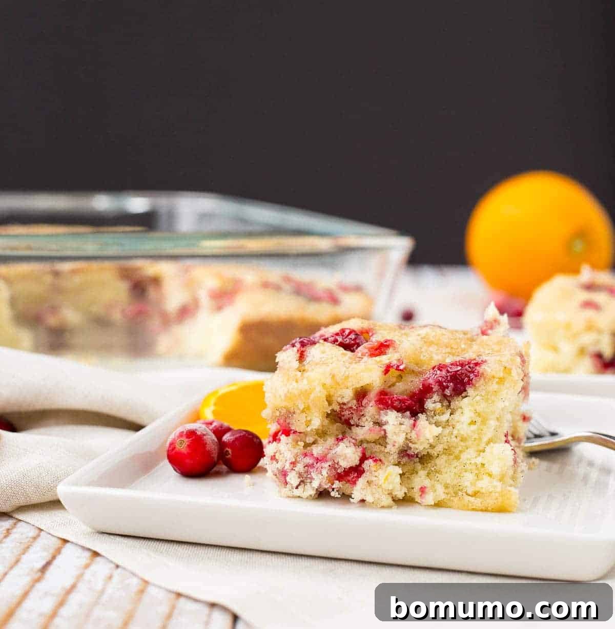Front view of a perfectly sliced piece of coffee cake, with the remaining cake resting in a clear glass baking dish in the soft-focus background.