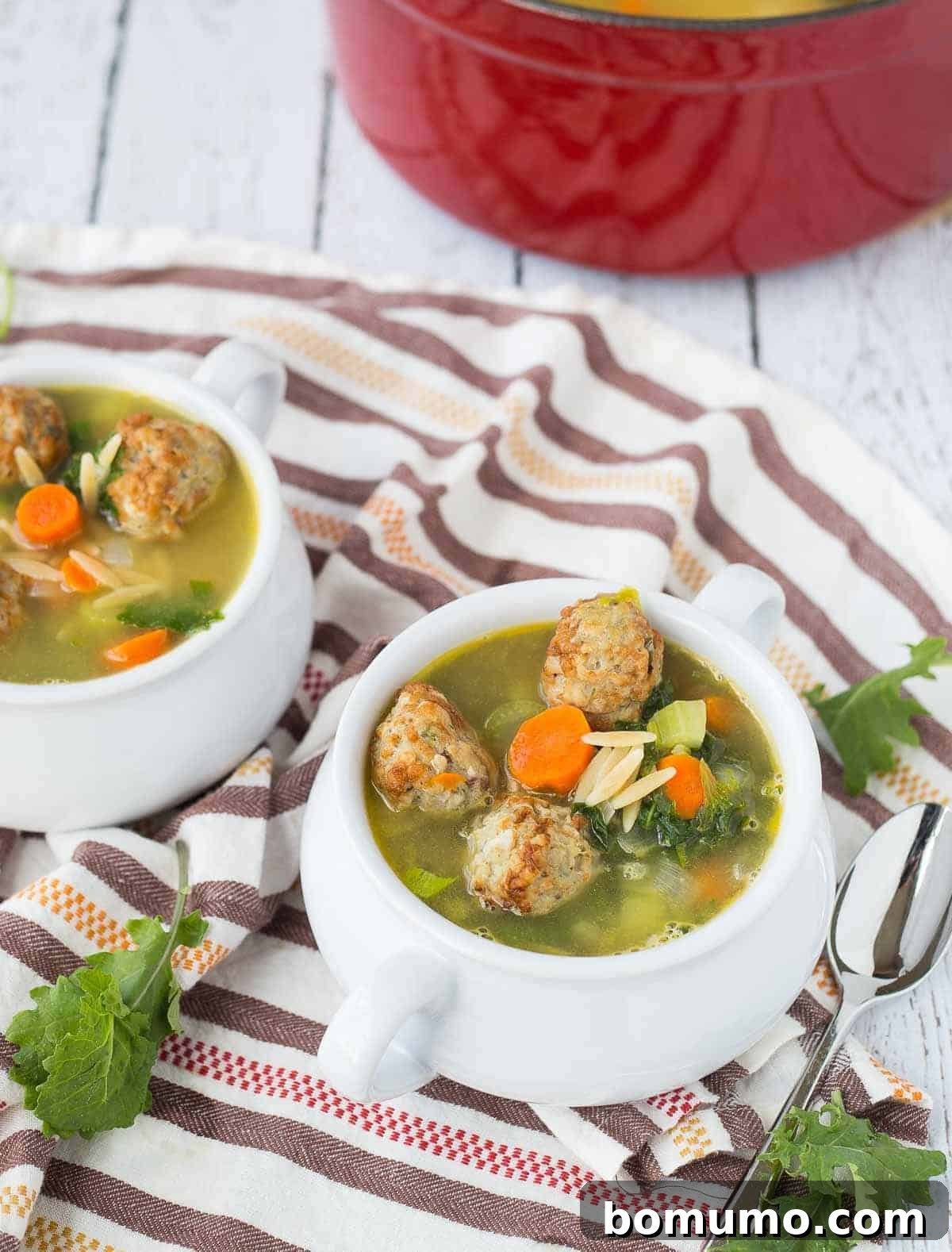Overhead shot of two servings of healthy meatball orzo soup in white bowls, placed on a brown striped cloth, ready to be enjoyed.