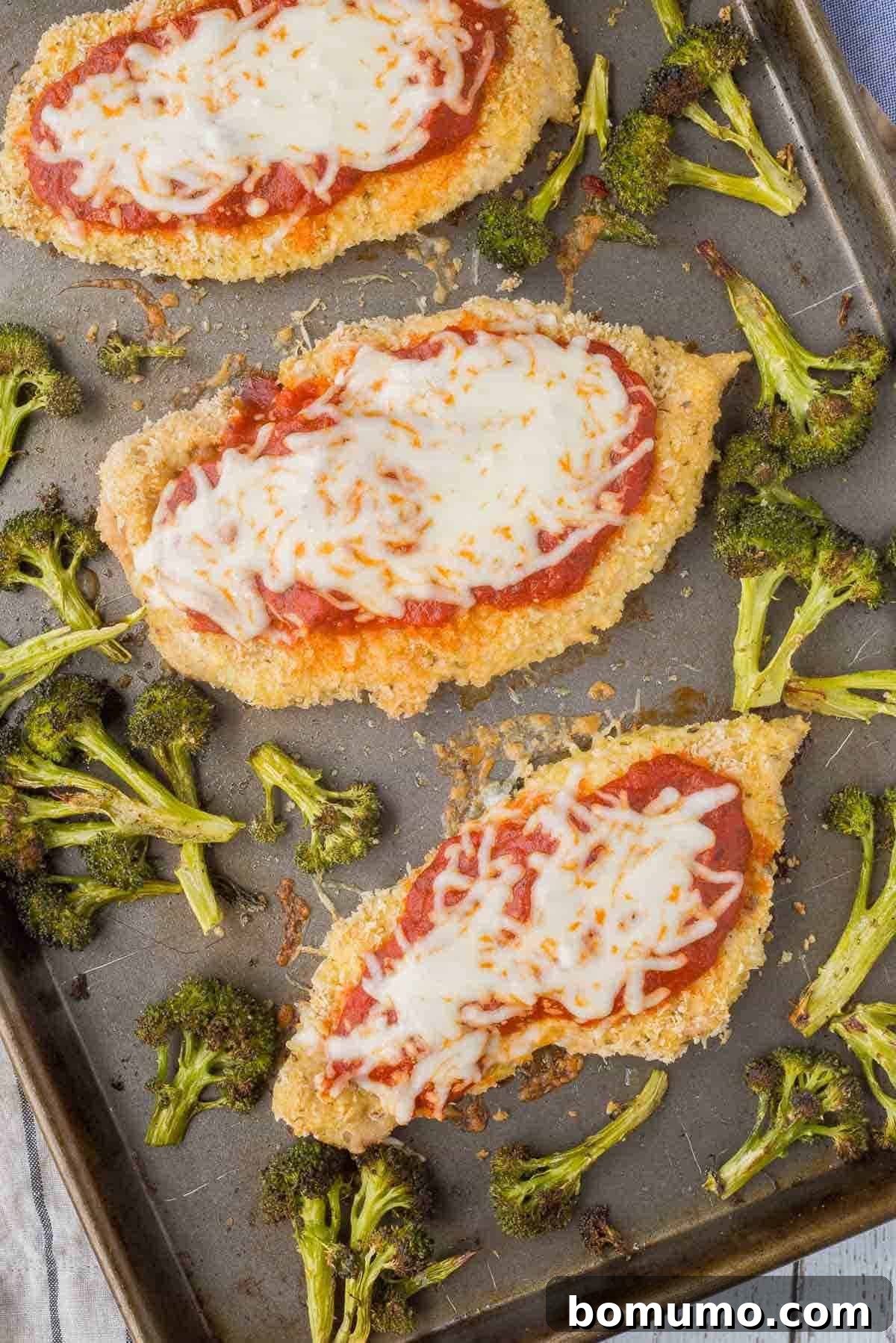 An appetizing overhead shot of golden-brown chicken Parmesan alongside perfectly roasted broccoli florets, served on a sheet pan, highlighting the ease of this one-pan dinner.