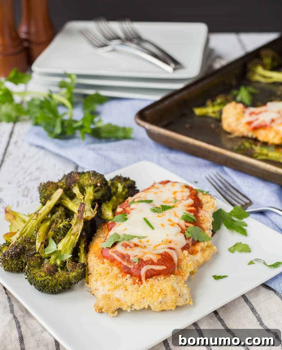 A single serving of golden-brown chicken Parmesan and roasted broccoli on a square white plate, with a fork, ready to be enjoyed.
