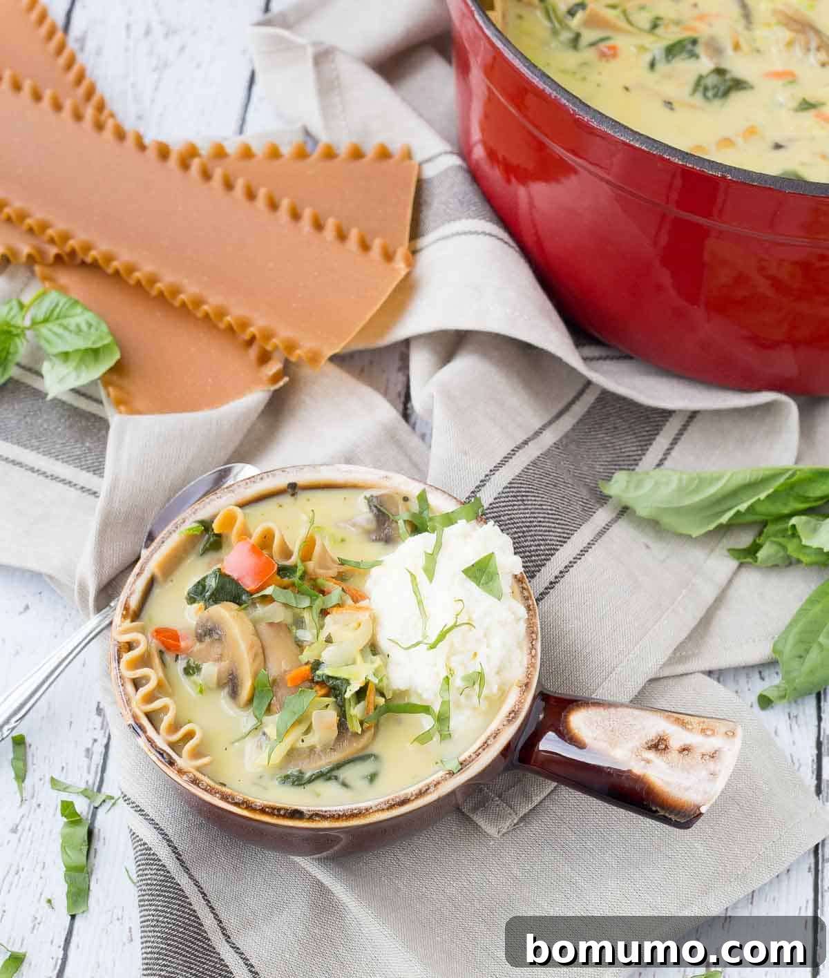 An inviting overhead shot of vegetarian lasagna soup served in a bowl, with a rich red Dutch oven prominently featured in the background, signifying the one-pot cooking method.