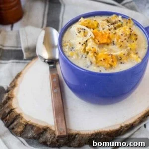 Chicken soup in blue mug with spoon on wood slice.