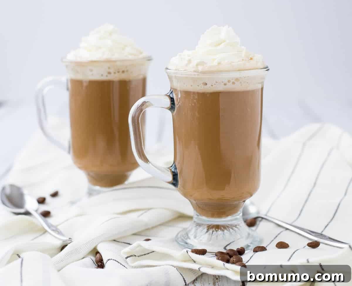 Front view of two mugs of white Russian hot chocolate with two spoons on cloth. 