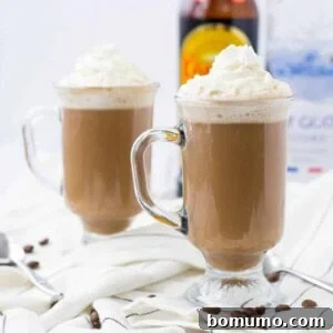Front view of two clear glass footed mugs containing White Russian hot chocolate garnished with whipped cream.