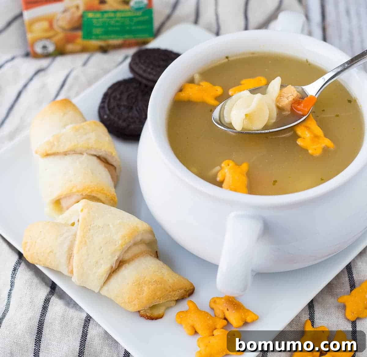 Sandwiches, soup, crackers, and cookies on square white plate.