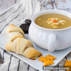 Sandwiches, crackers, bowl of soup, and cookies on square white plate.