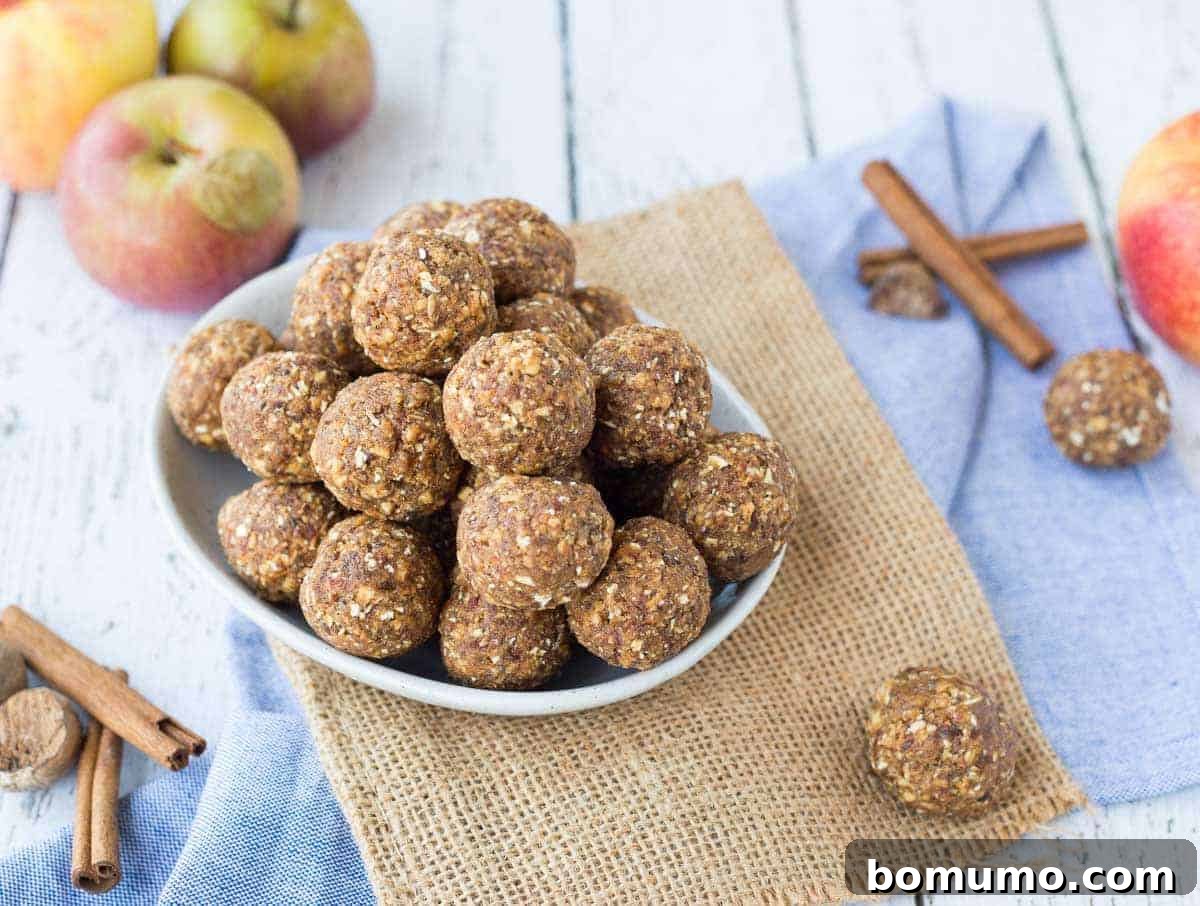 A beautifully composed shot featuring a bowl overflowing with homemade apple cinnamon energy bites, artfully arranged alongside fresh, crisp apples and aromatic cinnamon sticks, highlighting the natural ingredients.