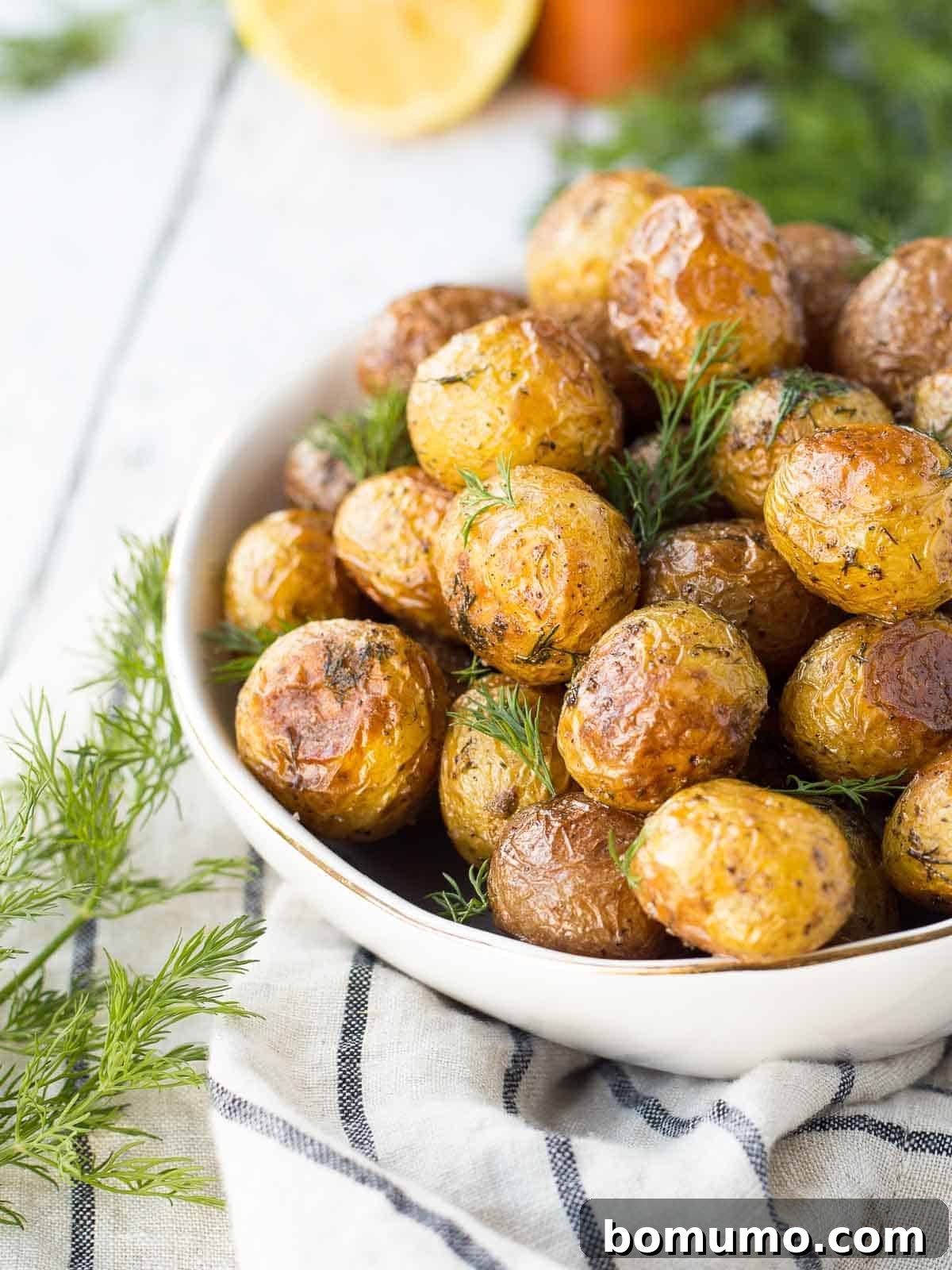A bowl of golden-brown dill roasted potatoes, garnished with fresh dill, ready to serve.