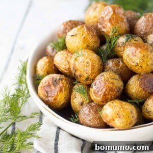 Partial image of roasted potatoes in round white serving dish, garnished with fresh dill.