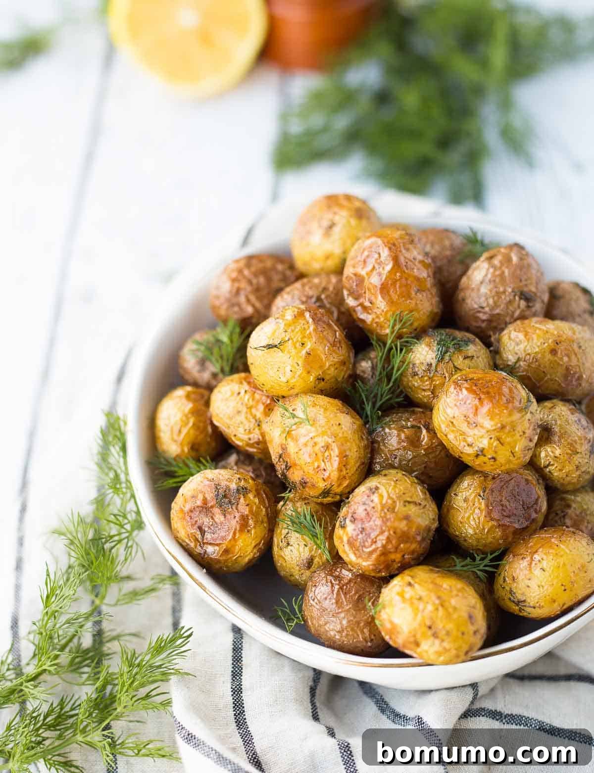 An overhead shot of vibrant dill roasted potatoes served in a elegant round white dish.