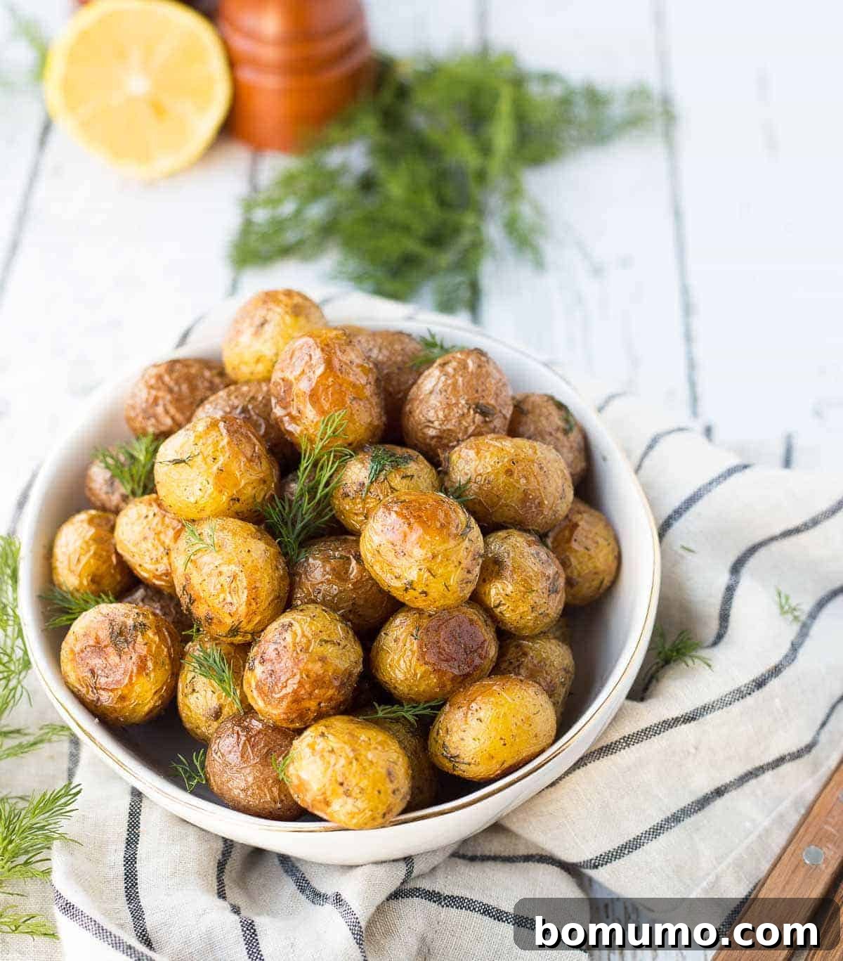 Overhead view of roasted potatoes generously garnished with fresh dill in a white serving bowl.