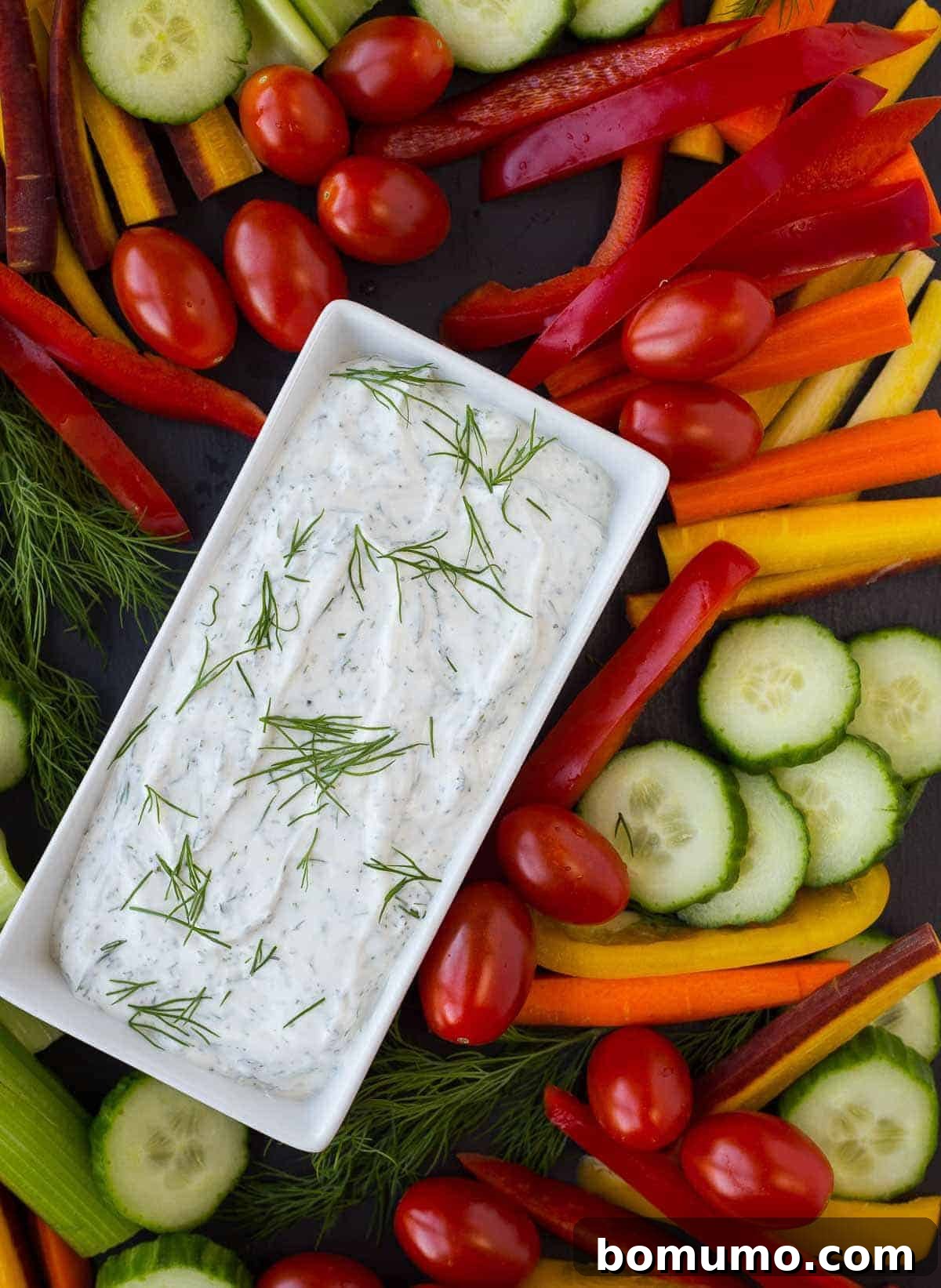 Fresh dill vegetable dip in a bowl, surrounded by a colorful array of fresh vegetables like carrots, celery, and bell peppers, ready for dipping.