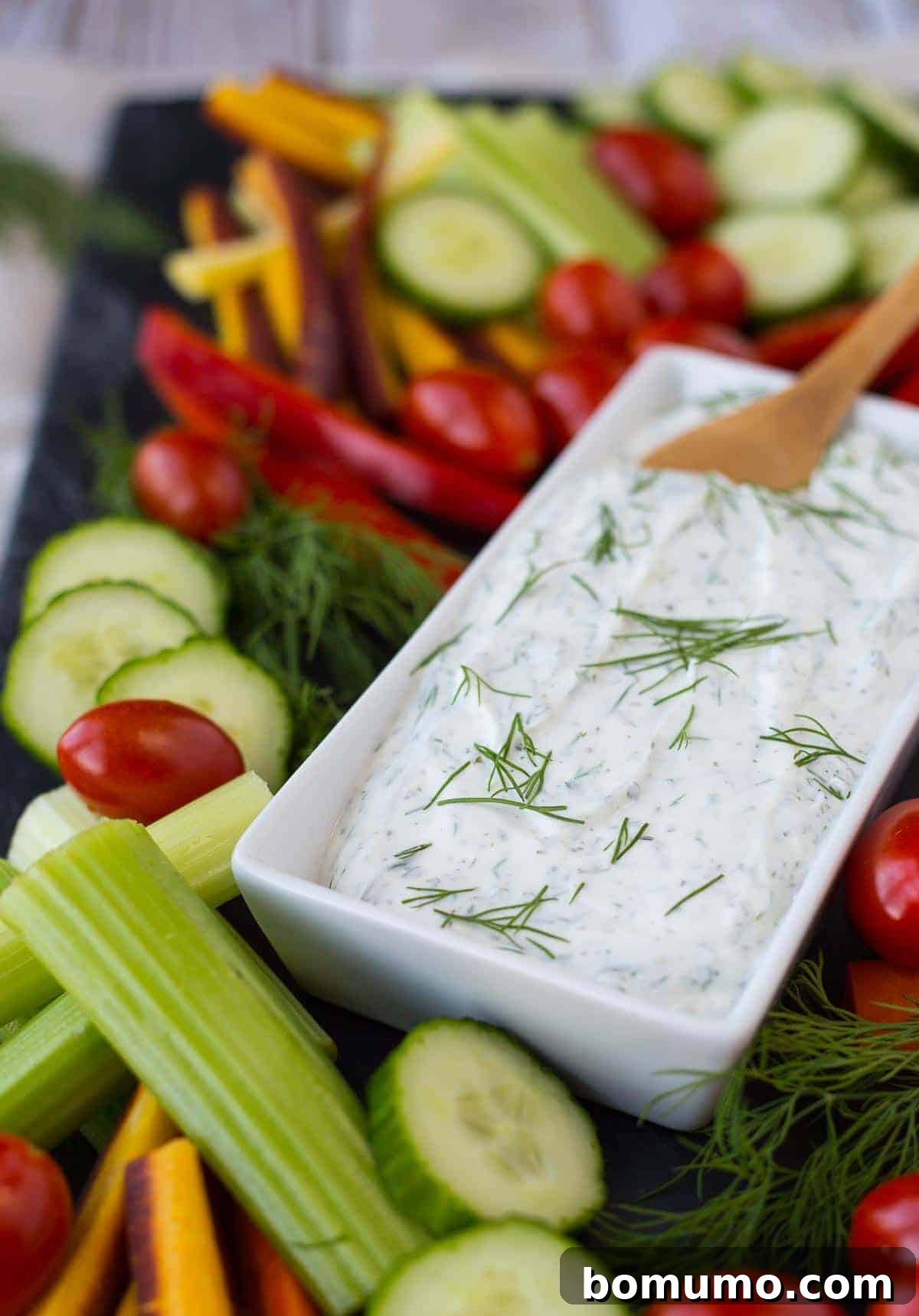 Close-up of creamy dill vegetable dip in a white bowl, garnished with fresh dill sprigs, ready to be served with fresh crudités.