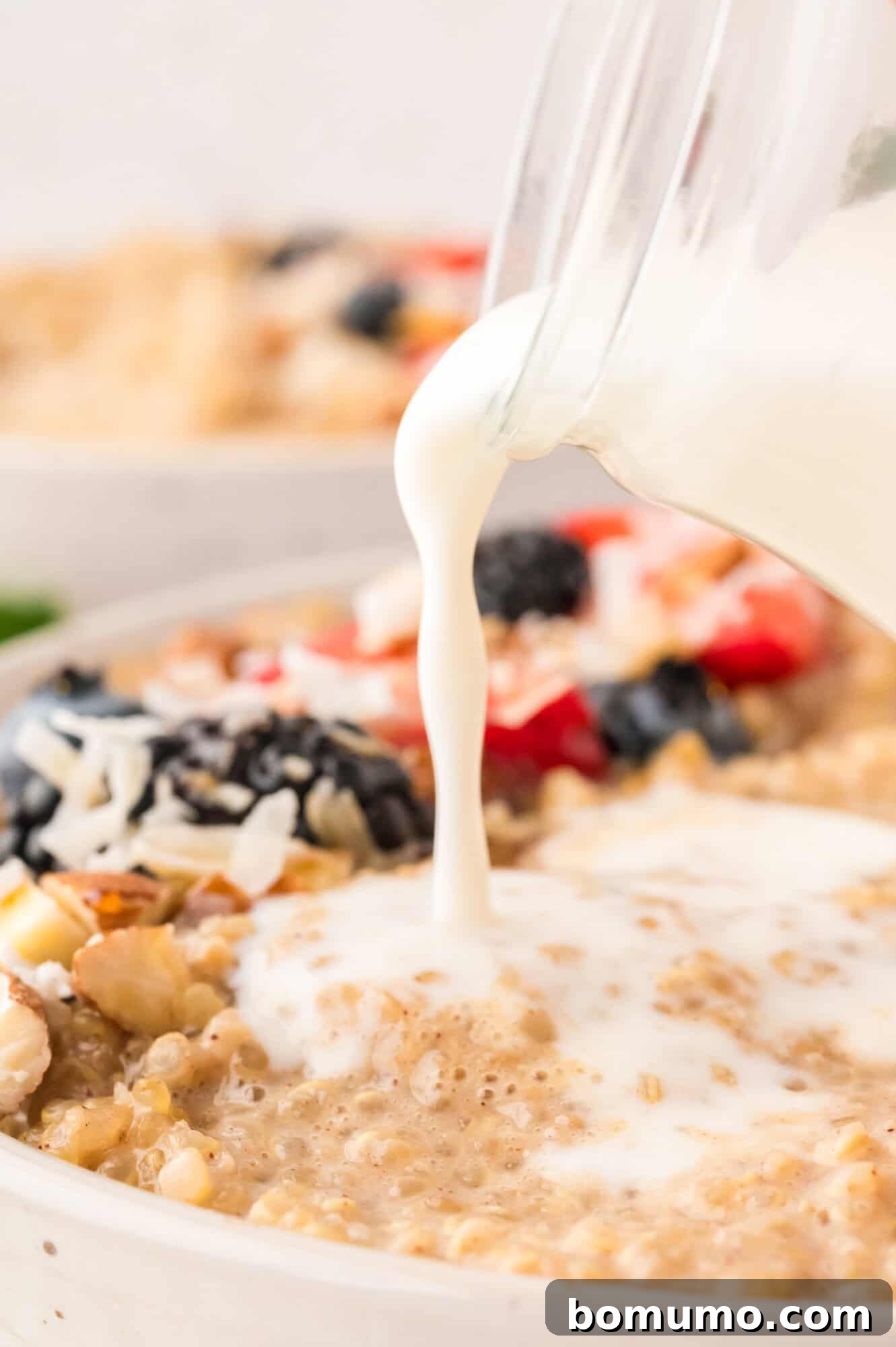 Fresh milk being gently poured into a bowl of cooked quinoa, enhancing its creaminess and preparing it for serving.