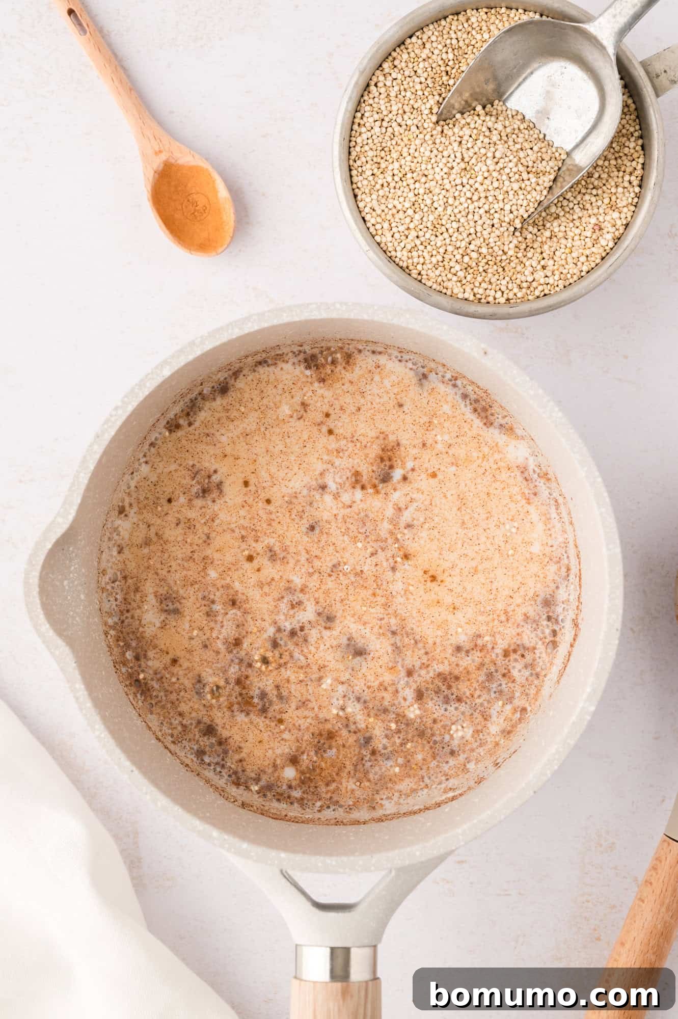 The quinoa and seasonings have been thoroughly mixed into the liquid, now gently simmering in an off-white saucepan, ready for cooking.