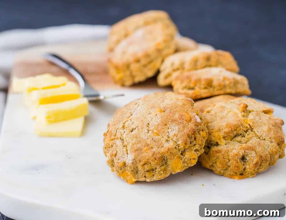 Close-up front view of a stack of golden-brown whole wheat biscuits, showing their flaky layers and the specks of cornmeal, cheddar, and black pepper.