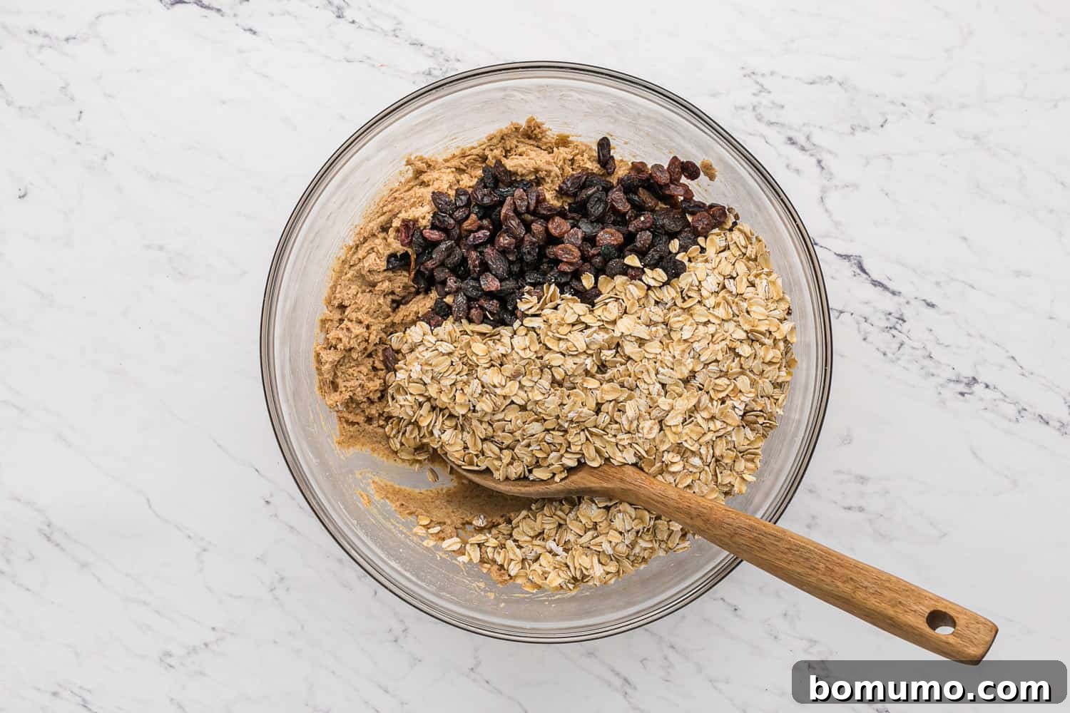 Old-fashioned rolled oats and raisins being folded into the prepared cookie dough.