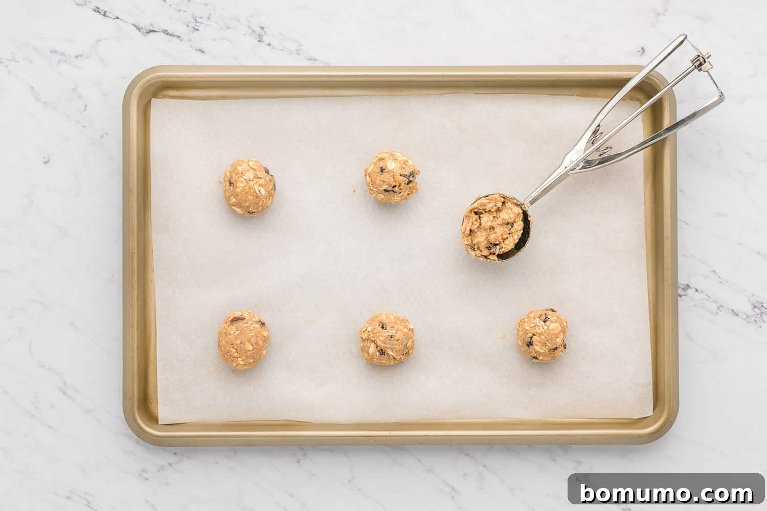 Unbaked oatmeal raisin cookie dough balls neatly arranged on a parchment-lined baking sheet.