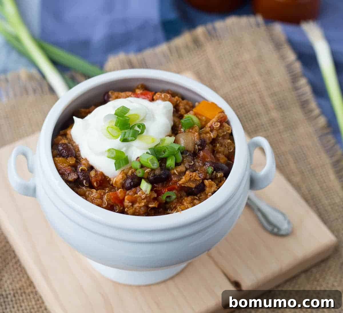 Close-up of turkey quinoa chili served in an elegant white bowl with a spoon, showcasing its rich texture and ingredients.