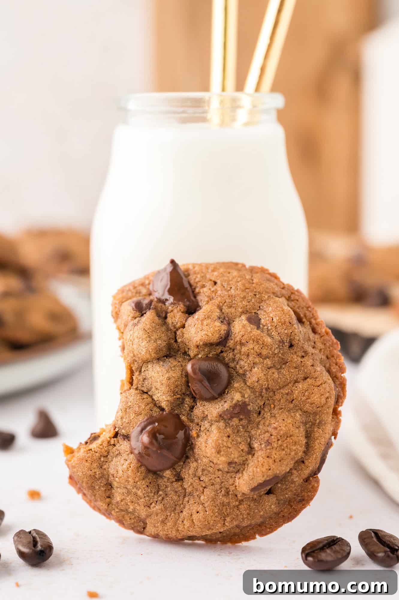 A perfectly baked coffee cookie, with a bite taken out, resting against a glass of milk.