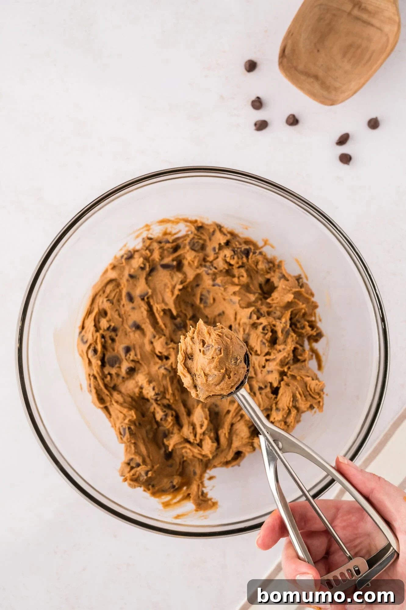 A scoop of coffee cookie dough being neatly placed onto a parchment-lined baking sheet.